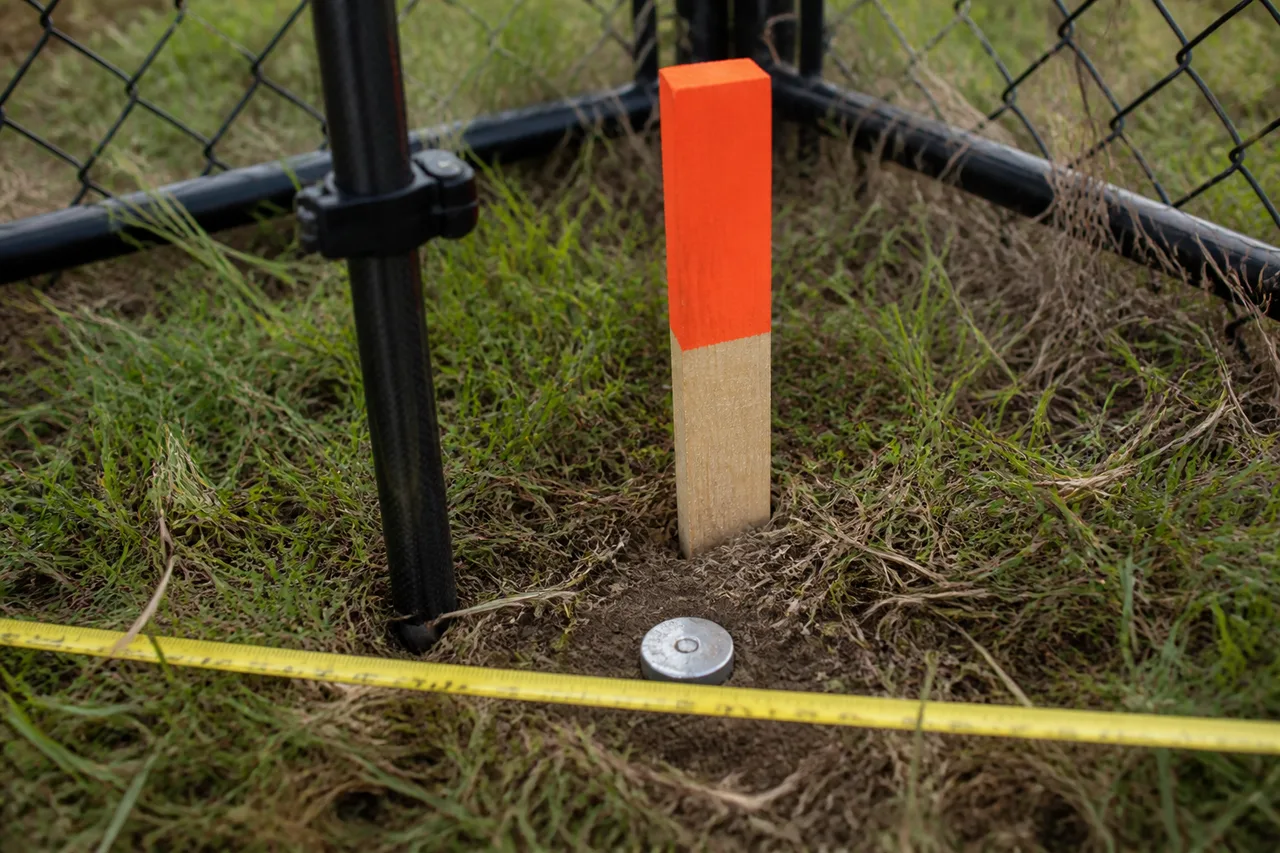 Detalle de un mojón de límite en la esquina de un terreno junto a una cinta métrica